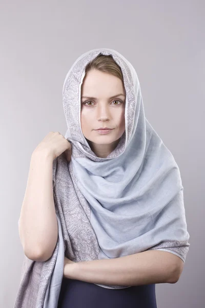 Härlig ung blondin i en blek blå scarf på huvudet på grå bakgrund — Stockfoto