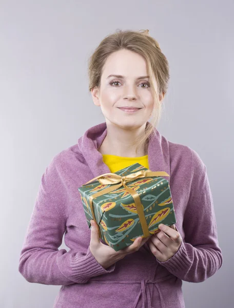 Mulher bonita segurando um presente brilhante no fundo cinza — Fotografia de Stock