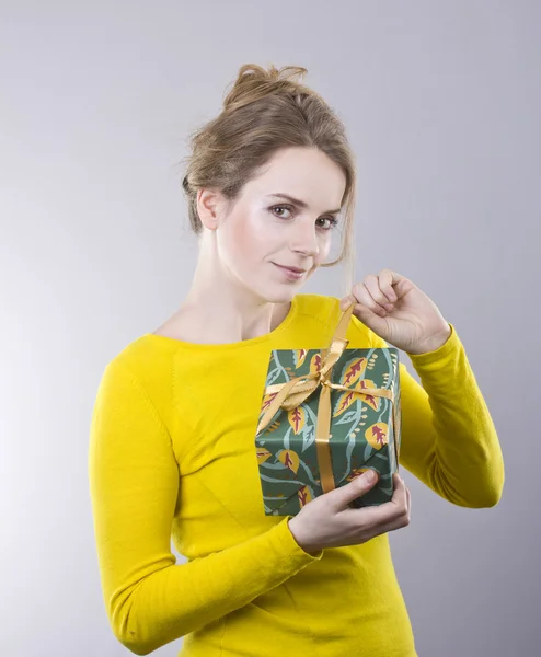 Beautiful young woman holding a bright gifts on gray background — Stock Photo, Image