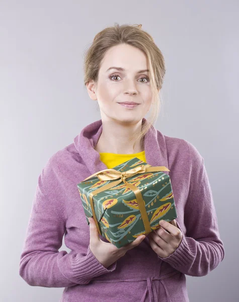 Hermosa mujer joven sosteniendo un brillante regalos sobre fondo gris — Foto de Stock