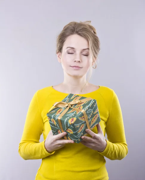 Hermosa mujer joven sosteniendo un brillante regalos sobre fondo gris — Foto de Stock