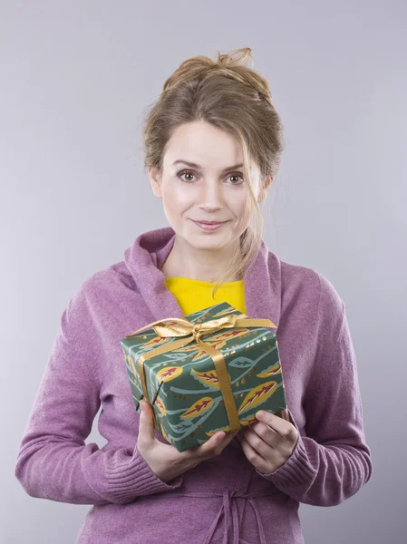 Beautiful young woman holding a bright gifts on gray background — Stock Photo, Image
