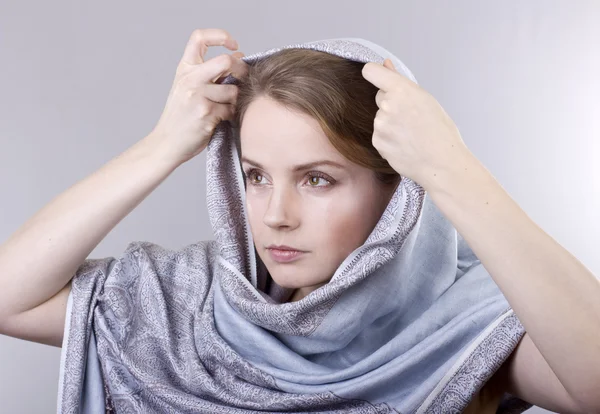 Hermosa joven rubia en una bufanda azul pálido en su cabeza sobre fondo gris — Foto de Stock