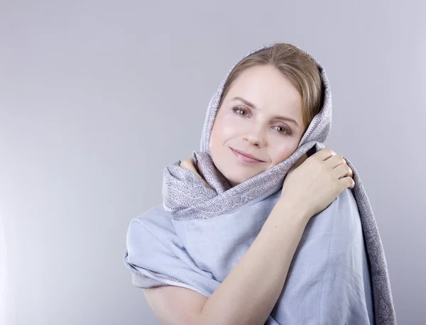 Schöne junge Blondine in einem blassblauen Schal auf ihrem Kopf auf grauem Hintergrund — Stockfoto