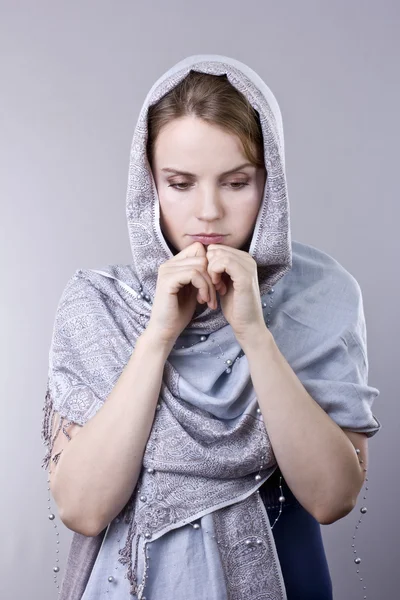 Mooie jonge blonde in een bleke blauwe sjaal op haar hoofd op grijze achtergrond — Stockfoto