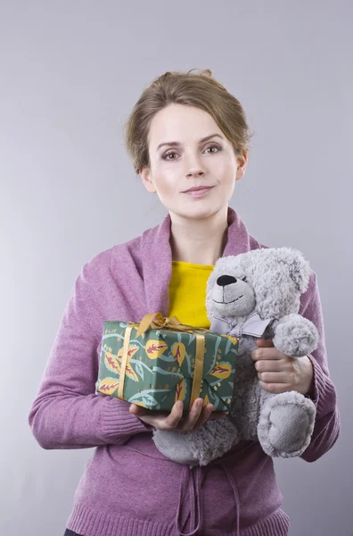 Mulher bonita segurando um presente brilhante no fundo cinza — Fotografia de Stock