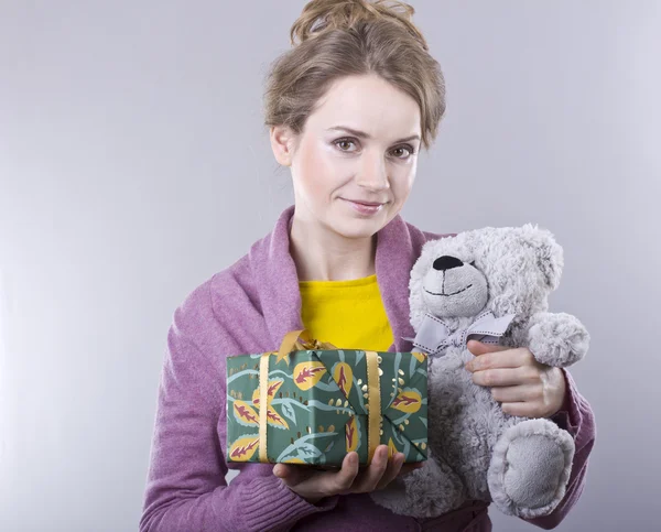 Beautiful young woman holding a bright gifts on gray background — Stock Photo, Image