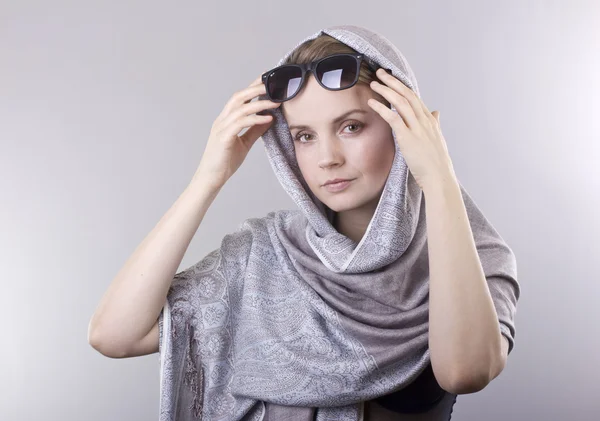 Hermosa mujer joven en un gris bordado mantones y gafas sobre fondo gris —  Fotos de Stock