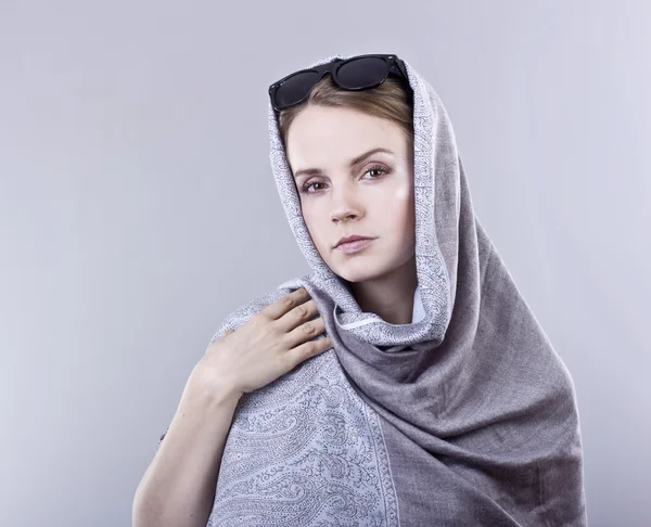 Beautiful young woman in a gray embroidered shawls and glasses on gray background — Stock Photo, Image