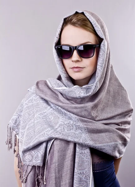 Beautiful young woman in a gray embroidered shawls and glasses on gray background — Stock Photo, Image