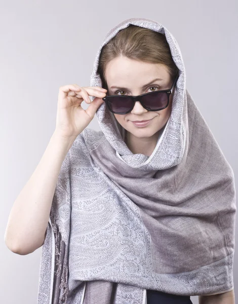 Krásná mladá žena v šedá vyšívané šály a brýle na šedém pozadí — Stock fotografie
