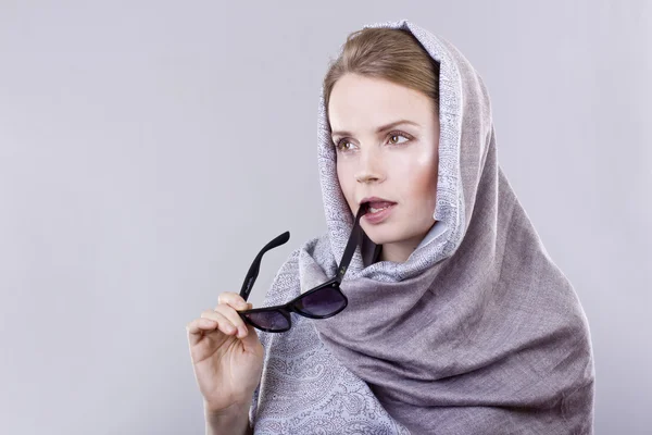 Beautiful young woman in a gray embroidered shawls and glasses on gray background — Stock Photo, Image