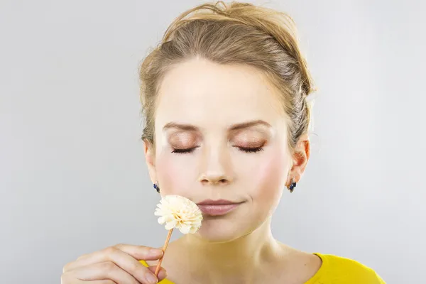 Schöne Blondine mit einer Blume in der Hand auf grauem Hintergrund — Stockfoto
