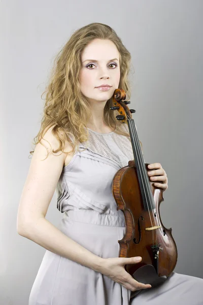 Beautiful curly blonde in gray evening dress with red violin in her hands — Stock Photo, Image