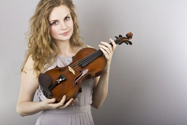 Vackra lockiga blondin i grå klänning med röda violin i hennes händer — Stockfoto