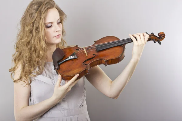 Linda loira encaracolada em vestido de noite cinza com violino vermelho em suas mãos — Fotografia de Stock