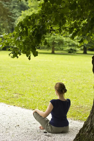 Skinny girl doing yoga under the green tree in the park — Stock Photo, Image