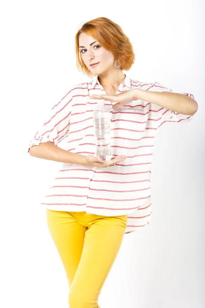 Hermosa joven con el pelo rojo corto bebiendo agua mineral de una botella. Retrato de una mujer sobre un fondo blanco — Foto de Stock