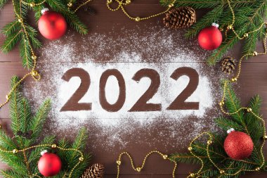 Köknar dalları kırmızı Noel topları ve kahverengi ahşap arka planda çam kozalaklarıyla süslenmiş 2022 sayısı. Yatay yönelim, üst görünüm.