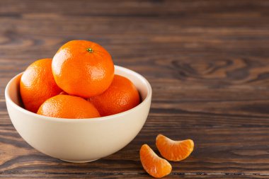 Tahta bir masada, bir kasede olgunlaşmış mandalinalar..