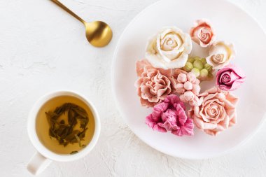 Bir fincan yeşil çayla birlikte bir tabakta duran marşmelovdan tatlı çiçekler. Yatay yönelim, üst görünüm.