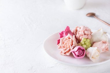 Beyaz fincanlı bir tabakta marşmelovdan gelen çok renkli tatlı güller. Yatay yönelim, boşluğu kopyala.