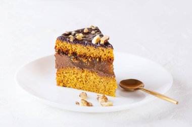 Bir dilim kabak turtası, çikolatalı ganache, portakallı kek ve beyaz tabakta fındık. Şeker, glüten ve laktozsuz vejetaryen.