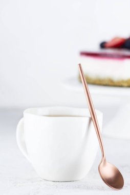 Pastanın arkasında çay kaşığı olan beyaz bir fincan çay..