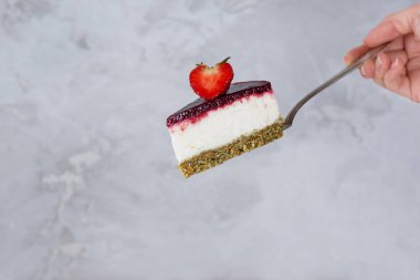 Elinde karnabahar ve gri bir arka planda böğürtlen olan bir parça kremalı pasta. Şeker, glüten, laktozsuz, vejetaryen.