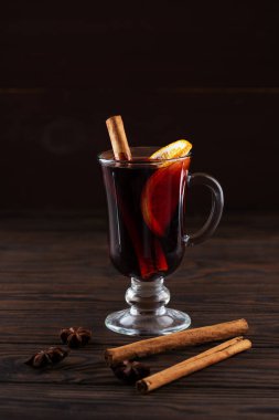 Koyu arkaplanda turuncu ve baharatlı bir bardakta sıcak şarap..