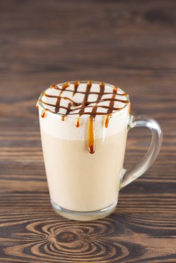 Tahta bir masada, cam bardakta hindistan cevizi kremalı vejetaryen karamel macchiato..