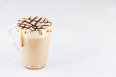 Beyaz bir masada cam bardakta vejetaryen karamel latte macchiato. Yatay yönelim, boşluğu kopyala.