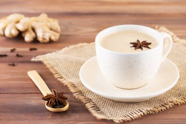 Masala tea with milk, ginger root and spices in a mug on a wooden table.