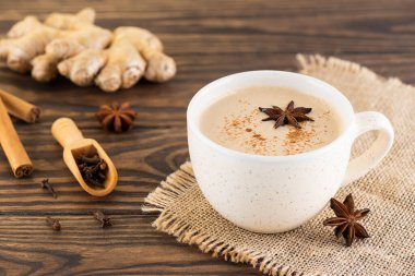Vegan masala tea with milk, ginger root and spices in a mug on a wooden table.