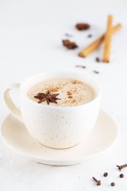 Masala tea with milk, ginger root and spices in a mug on a table.