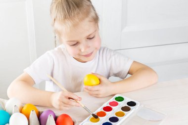 Şirin küçük kız fırçayla yumurta boyuyor. Paskalya konsepti.