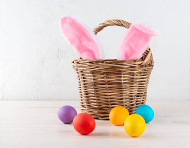 Hasır sepetli Paskalya yumurtaları ve tahta masada tavşan kulakları.. 