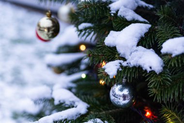 Dışarıda karların altında cam toplar ve çelenklerle süslenmiş Noel ağacı.