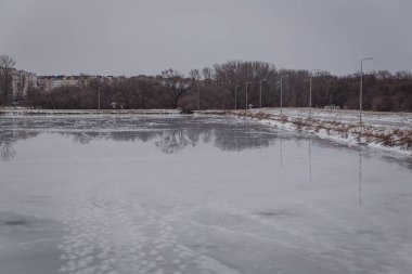 winter landscape in warm weather view of a frozen lake covered with melted snow gray sky bare trees
