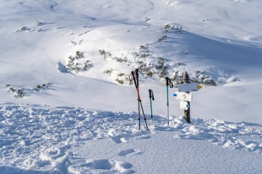 Dağların tepesindeki tabelanın yanındaki karda turist çubukları.