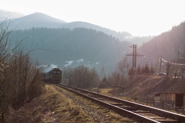 Eski yolcu treni, Carpathian dağları arasında ilkbaharın başlarında gün batımında tren yolunda ilerliyor.