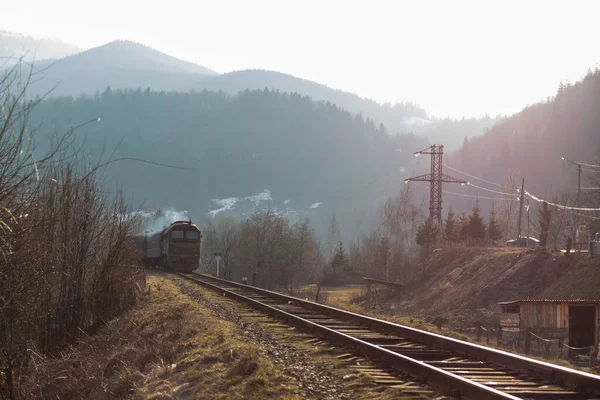 Eski yolcu treni, Carpathian dağları arasında ilkbaharın başlarında gün batımında tren yolunda ilerliyor.