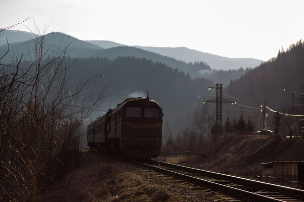 Eski yolcu treni, Carpathian dağları arasında ilkbaharın başlarında gün batımında tren yolunda ilerliyor.