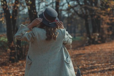 Beyaz önlüklü, ince şapkalı, omuzlarında kırmızı çantalı mutlu kıvırcık kız, Sunn 'daki sonbahar parkında sarı yaprakların ortasında döner.