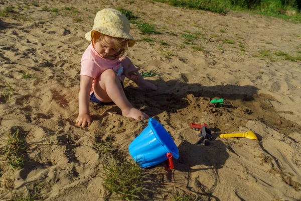 little girl on the beach in a yellow hat having fun playing with sand girl wearing a pink t-shirt and blue shorts girl very happy and interested in sunny warm weather in summer on vacation