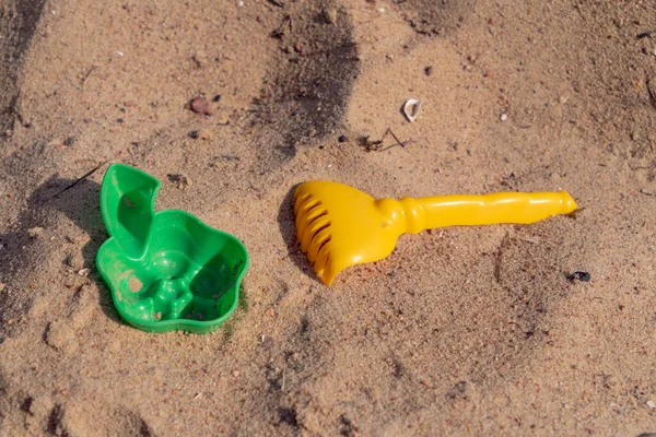 children\'s plastic rakes and flower shape for playing with sand lie on warm yellow sand on the beach in hot sunny weather top view