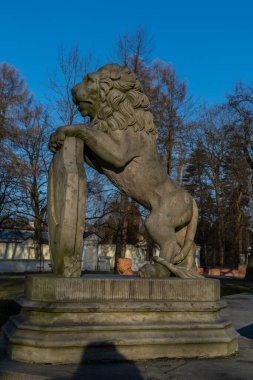 Polonya 'nın Varşova kentindeki Wilanw Sarayı' nın yakınındaki eski, güneşli hava heykelinde, kaidede kalkanı olan beton aslan heykeli.