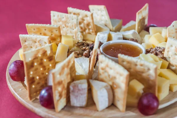 Diferentes variedades de queso con uvas, galletas saladas, frutos secos y ho —  Fotos de Stock