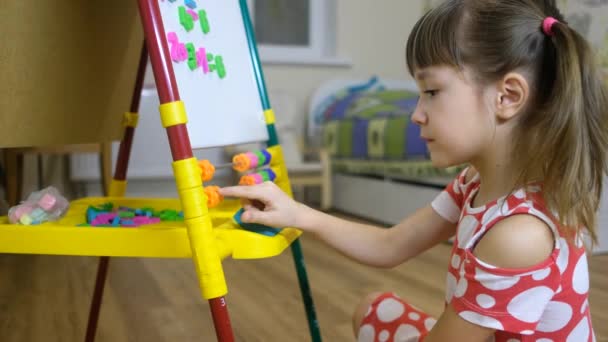 Anak gadis menggunakan papan magnet untuk belajar huruf dan angka di rumah — Stok Video
