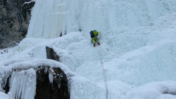 Alpinist man med is verktyg yxa klättra ett fruset vattenfall, en stor vägg av is — Stockvideo